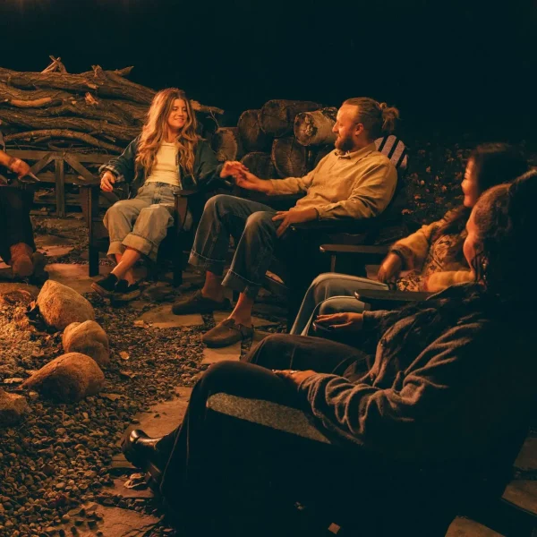 A group of men and women sitting in Adirondack chairs around a fire.